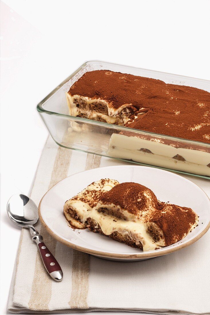 Tiramisu in a glass dish with a slice on a plate