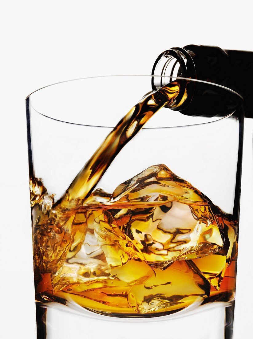 Whisky being poured into a glass over ice