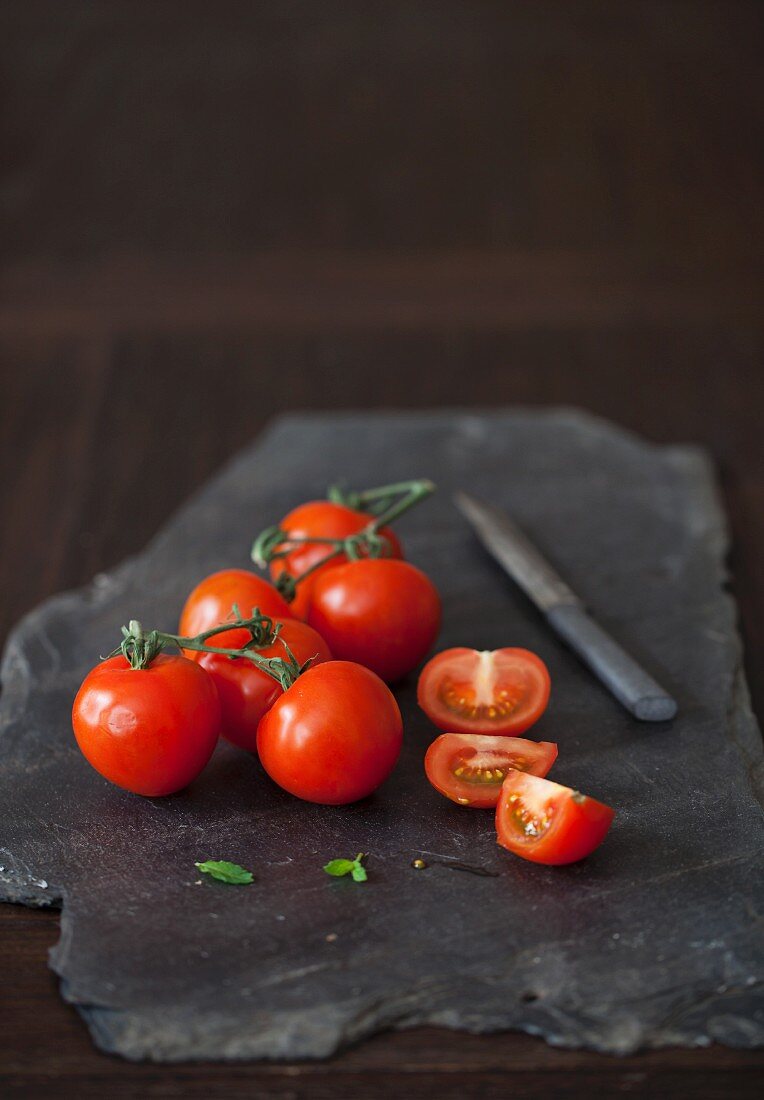 Tomatoes, whole and halved, on a black stone