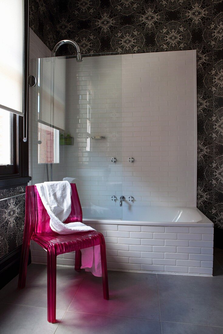 Pinkfarbener Kunststoff-Stuhl vor Badewanne mit Glas-Trennwand, an Wand Tapete mit sphärischem Sternenmuster