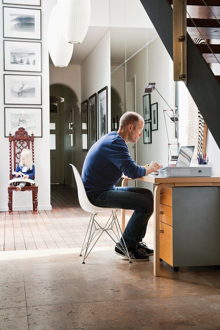 Mann auf Klassikerstuhl an Home Office Platz bei der Arbeit im Dielenbereich unter der Treppe