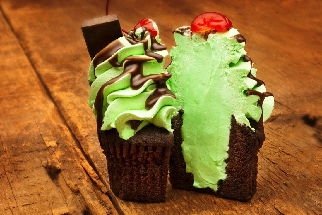 A chocolate cupcake decorated with mint cream, chocolate sauce and a cherry on a wooden table