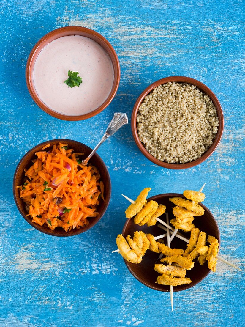 Chicken tandoori skewers with quinoa, carrot salad and raita in small bowls