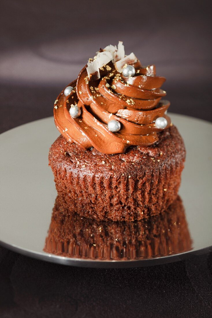 Edler Schokoladen-Cupcake mit silbernen Zuckerperlen, weissen Schokoraspeln und Goldpuder