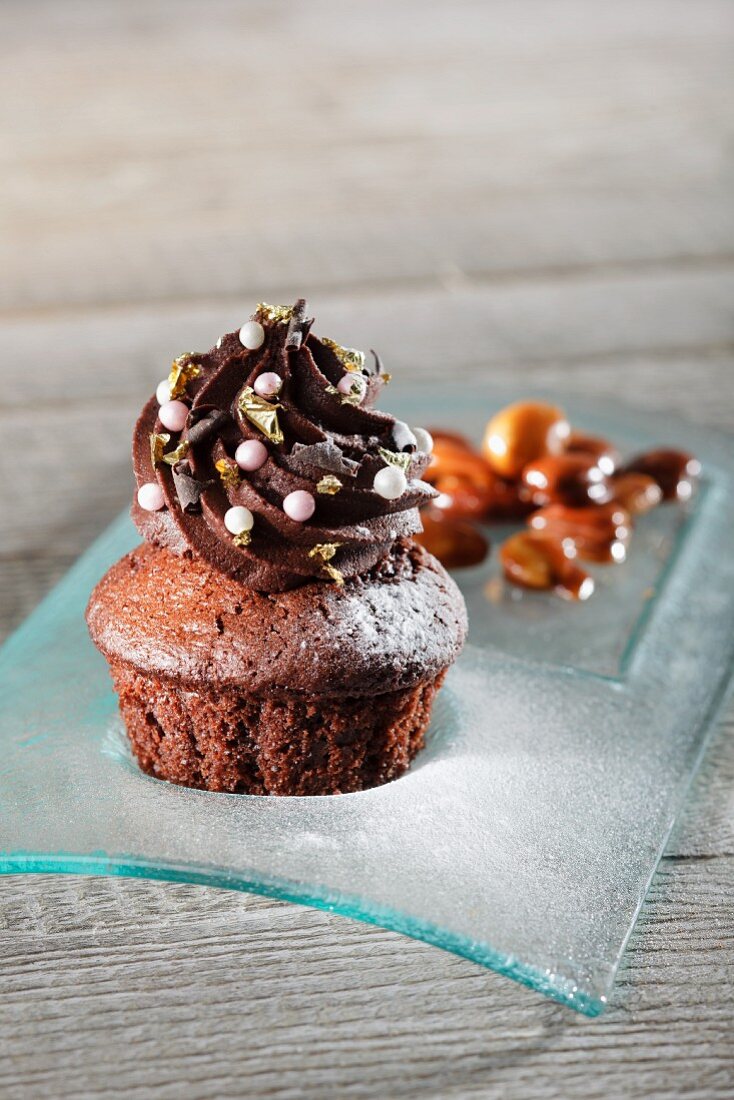 A chocolate cupcake decorated with sugar pearls and gold leaf