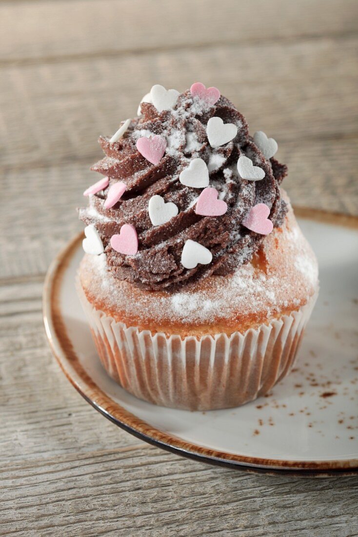 A cupcake decorated with chocolate buttercream and sugar hearts