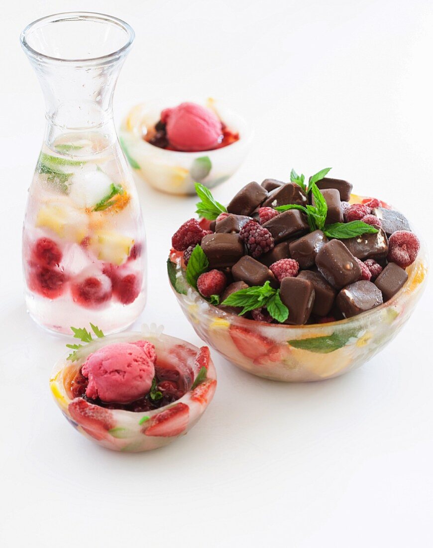 Ice bowls filled with frozen chocolates and raspberry ice cream with a carafe of water and fruit ice cubes in the background