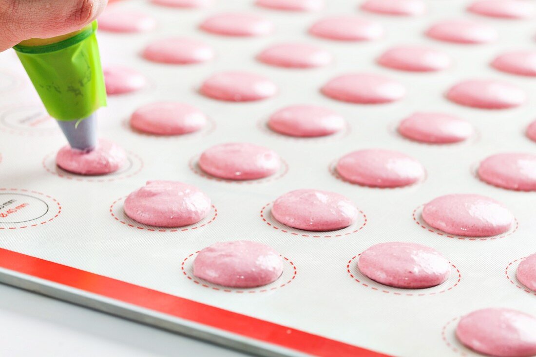 Teig für rosa Macarons mit Spritzbeutel auf Backpapier setzen