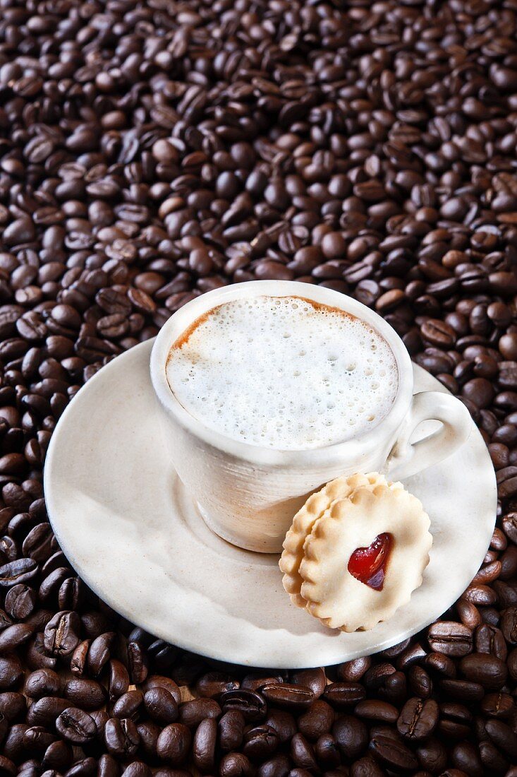 A cappuccino on coffee beans with a jam sandwich biscuit