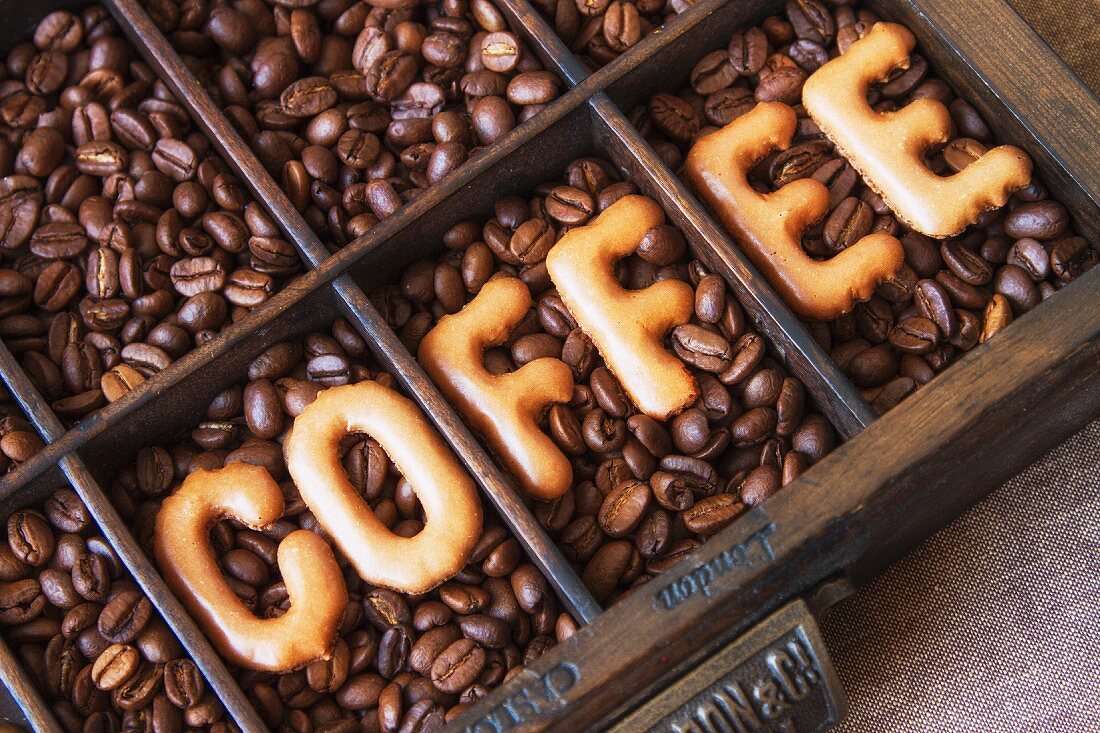 The word 'coffee' written using alphabet biscuits on top of coffee beans