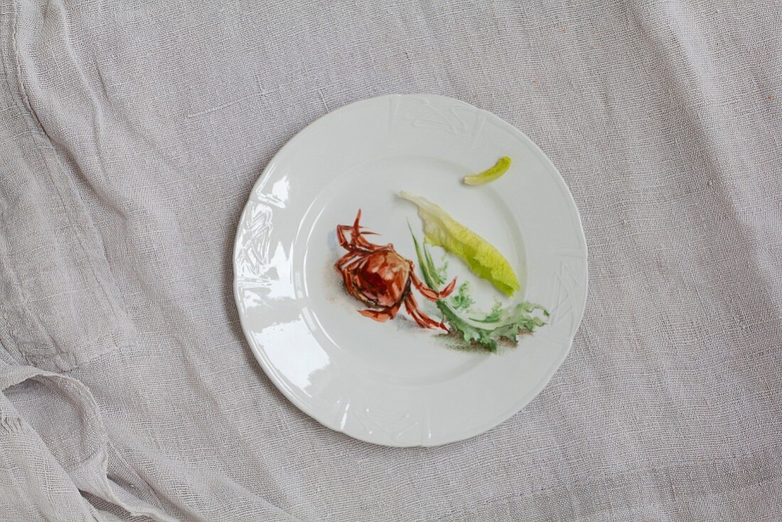 Weisser Porzellanteller mit rotem Taschenkrebs und verschiedenen Salatblättern