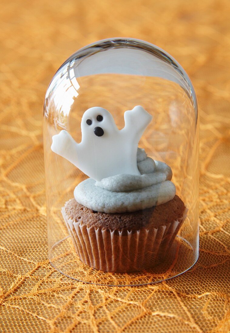 A cupcake decorated with a ghost for Halloween under a glass cloche
