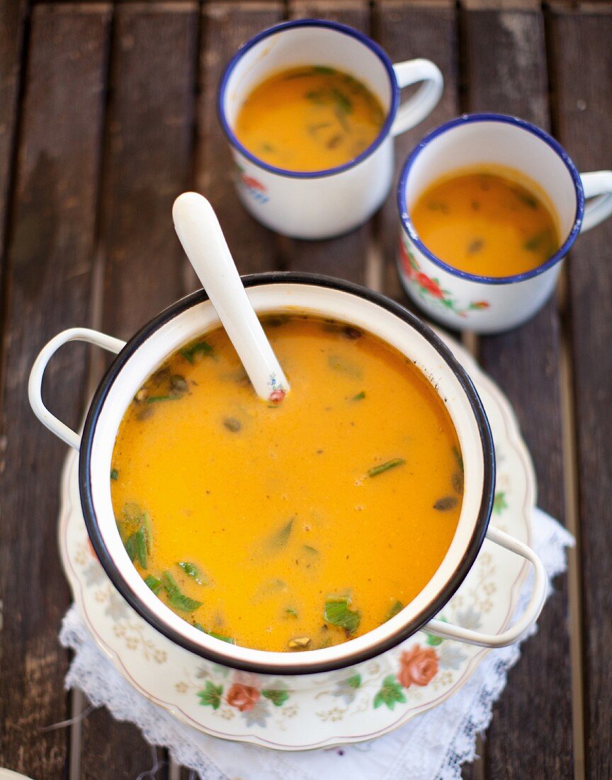 Sweet potato soup with ginger in an enamel pot with two cups of soup in the background