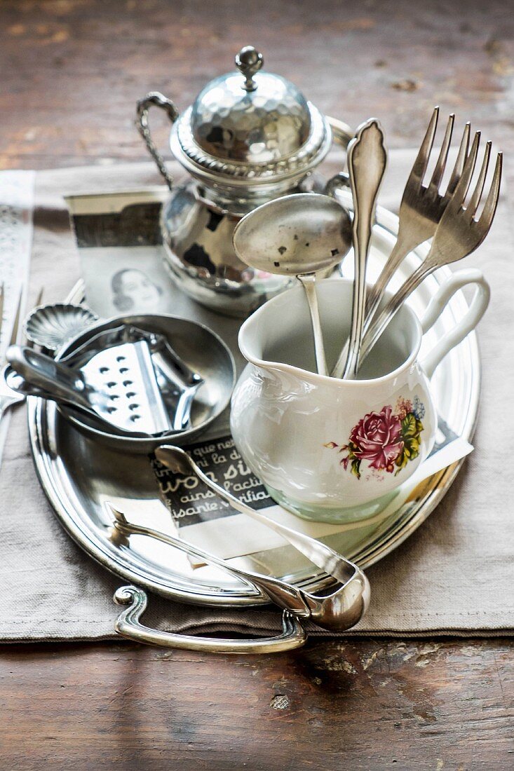 Silver cutlery in a porcelain jug and a lemon press on a tray