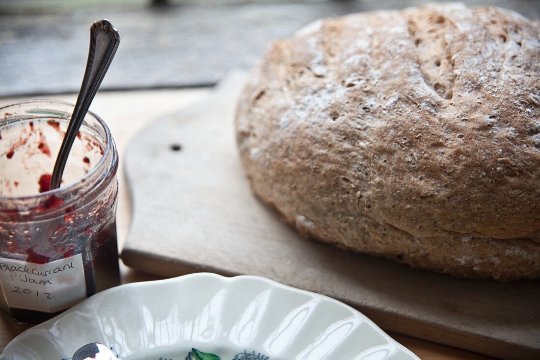 A whole loaf of homemade wholemeal bread and jam on a wooden board