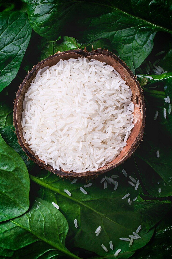 Jasmine rice in a coconut shell on a bed of spinach leaves