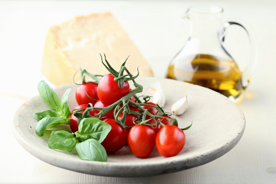 Tomaten auf Steinteller mit Basilikum und Knoblauch vor Ölkaraffe und Parmesan