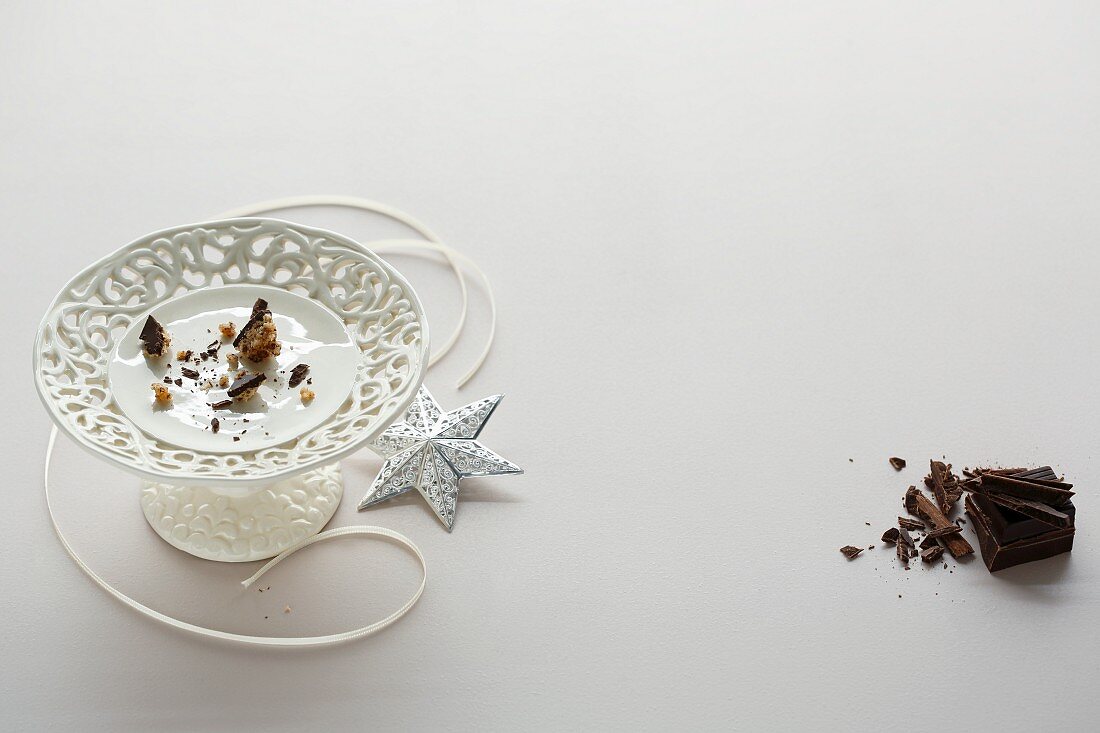 Crumbs on a white cake stand, a ribbon and a silver decorative star with grated chocolate to the left