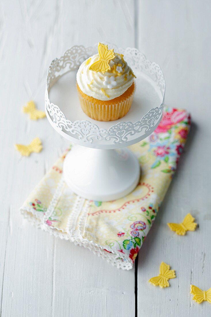 A cupcake decorated with a yellow butterfly on a white cake stand