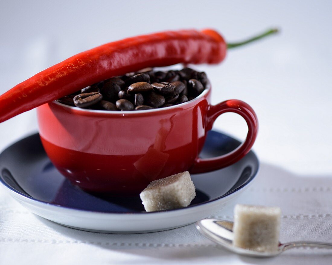 Kaffeebohnen in roter Tasse mit Chilischote und Zuckerwürfeln