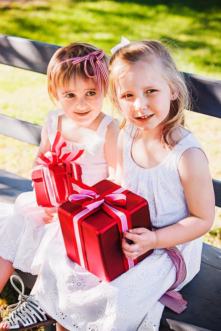 Two little girls sitting with presents on wooden bench in garden