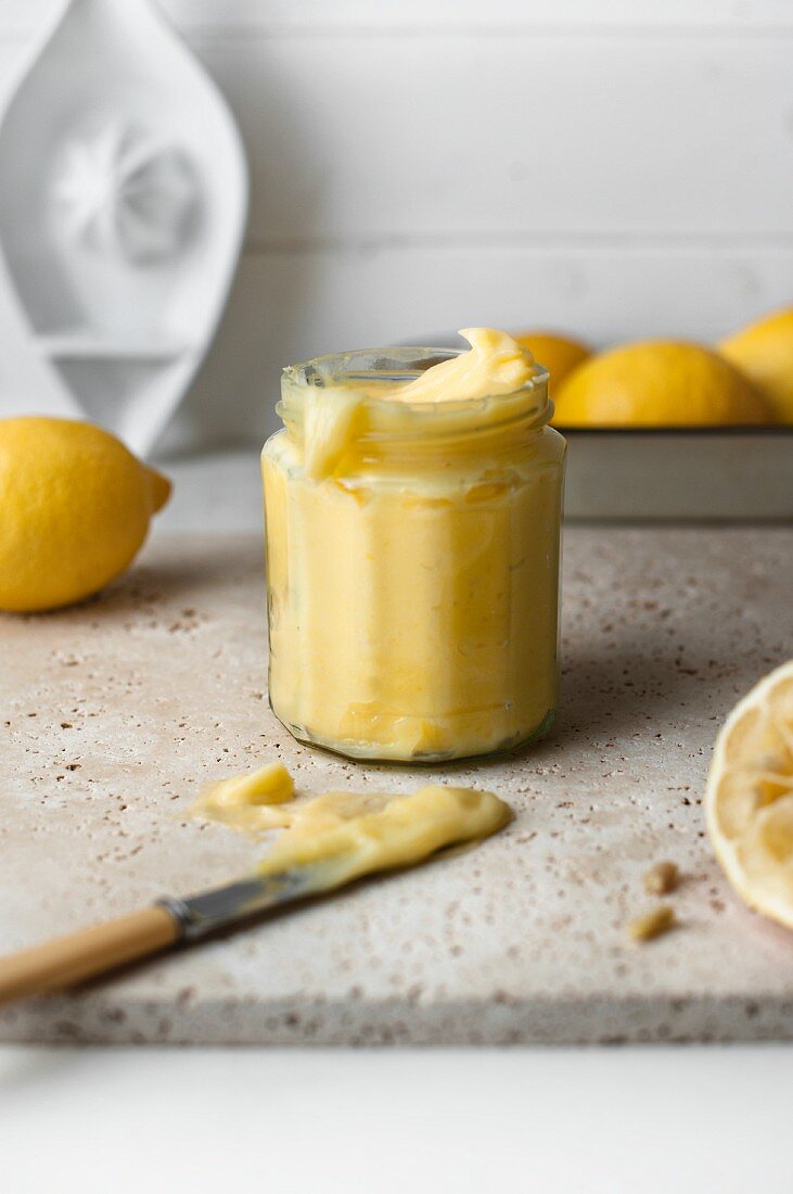 Zitronencreme in Marmeladenglas und frische Zitronen in einer Schale