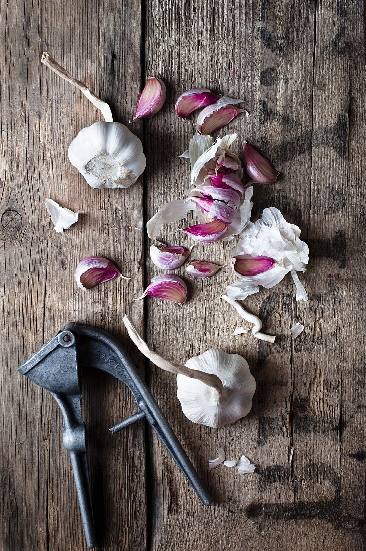 Garlic scattered on a rustic wooden surface with an old garlic press