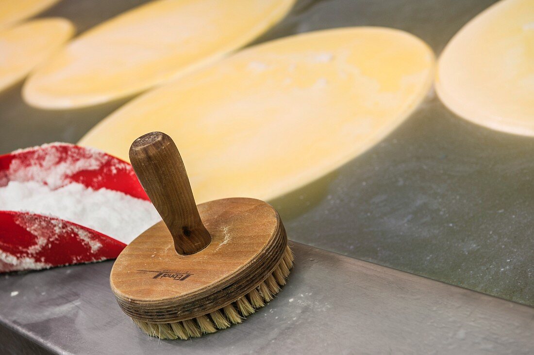 Wheels of cheese in brine being brushed to created a rind