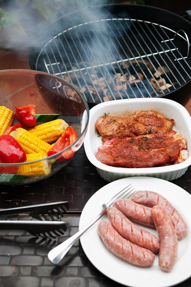 Marinated pork steaks, sausages and vegetables in front of a hot barbecue