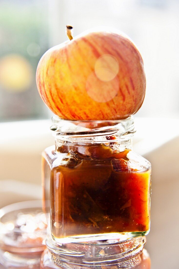 A jar of apple chutney with an apple on top in autumnal sunlight