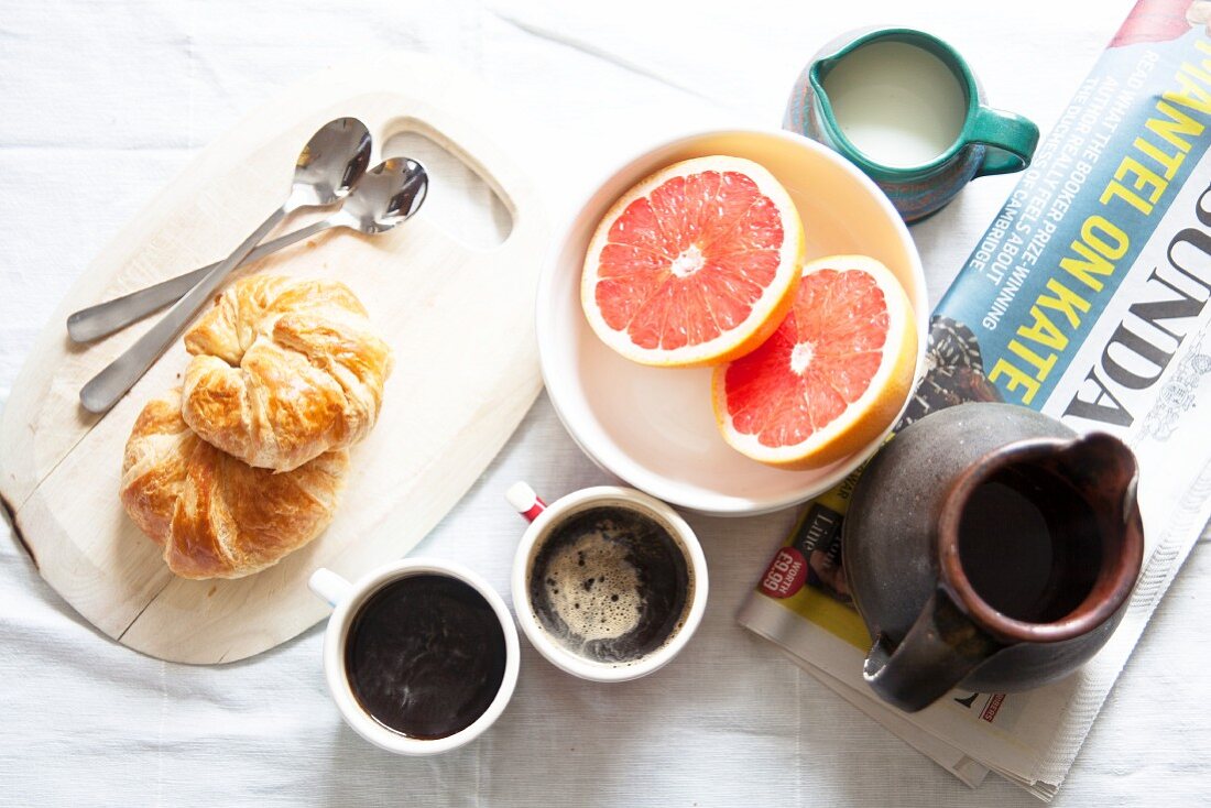 Frühstück mit Croissants, Kaffee, Grapefruits und Zeitung
