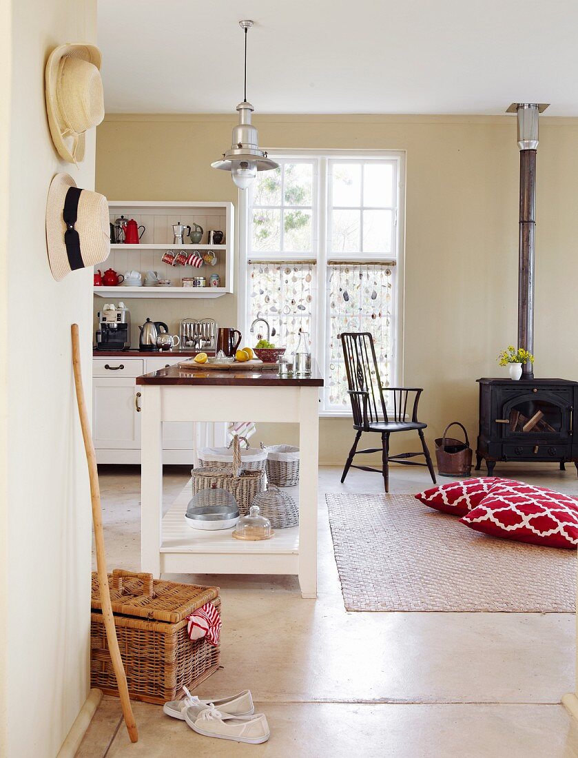 Island counter in open-plan kitchen with floor cushions in front of log-burner in rustic interior