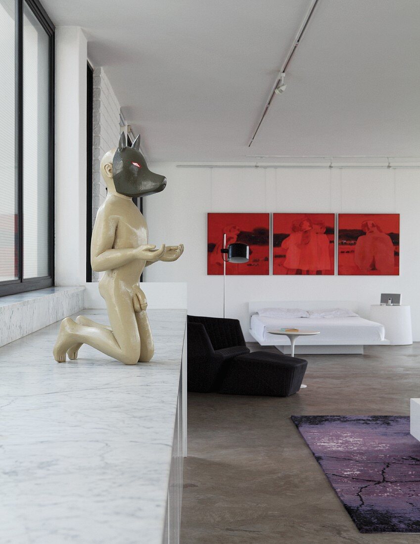 Menschenskulptur mit Tiermaske auf Marmorplatte mit Unterschränken, im Hintergrund ein rotes Triptychon in Loftwohnung