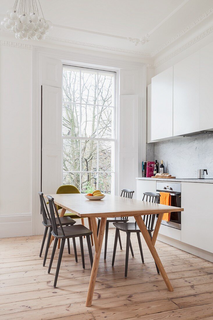 Simple white fitted kitchen in renovated period building with floor-to-ceiling lattice window, stripped wooden floor and retro dining set