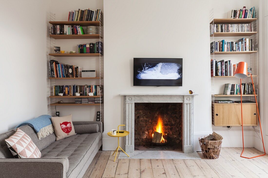 Gemütliches Kaminzimmer in renovierter Altbauwohnung mit loderndem Feuer, Wandbildschirm und symmetrisch angeordneten Bücherregalen