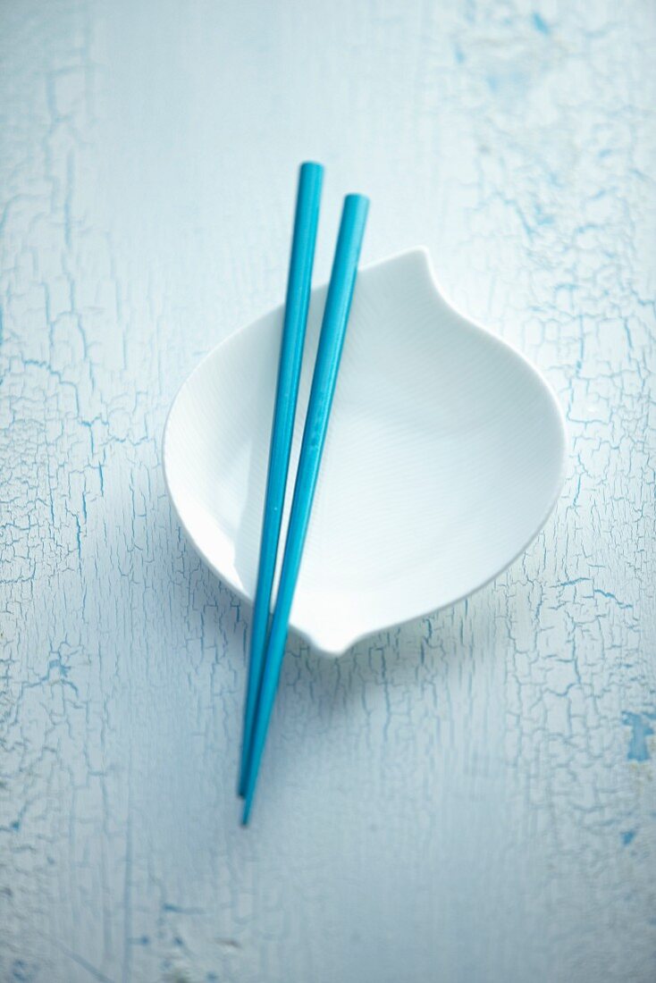 Blue chopsticks balanced over a white bowl