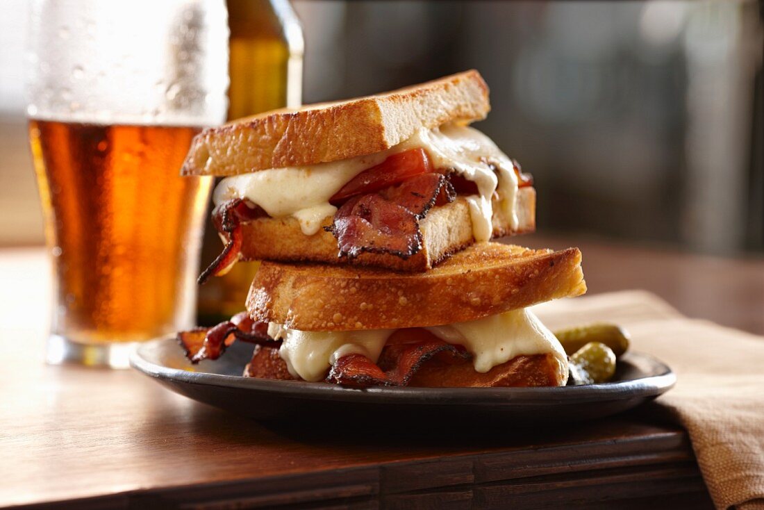 A toasted bacon and cheese sandwich with beer