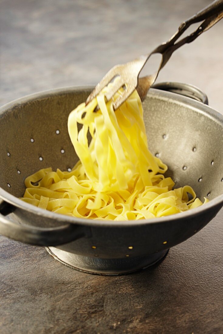 Linguine in a colander with pasta tongs
