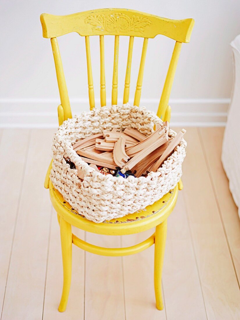 Wooden toys in basket on yellow-painted Thonet chair