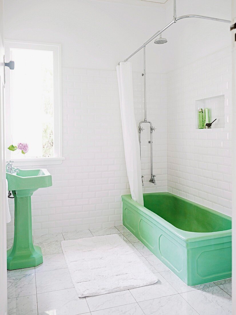 Green vintage pedestal sink and vintage bathtub with shower curtain in white-tiles bathroom with marble floor