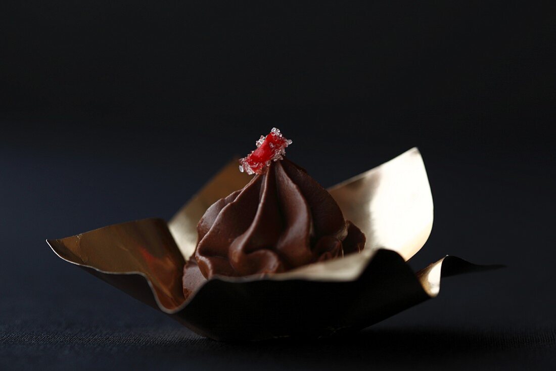 A dark chocolate praline on gold foil decorated with a piece of chilli