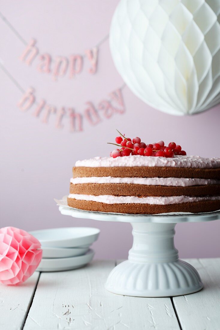 A redcurrant cake on a cake stand with the word 'Happy Birthday in the background