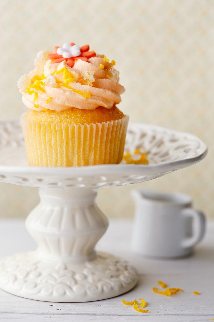 An orange and ginger cupcake on a cake stand with orange zest