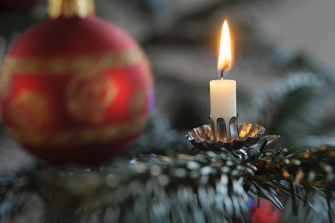 A Christmas decoration with s candle and a bauble