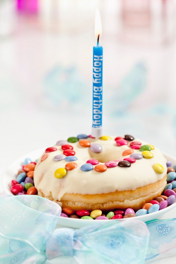 A doughnut decorated with colourful chocolate beans and a birthday candle