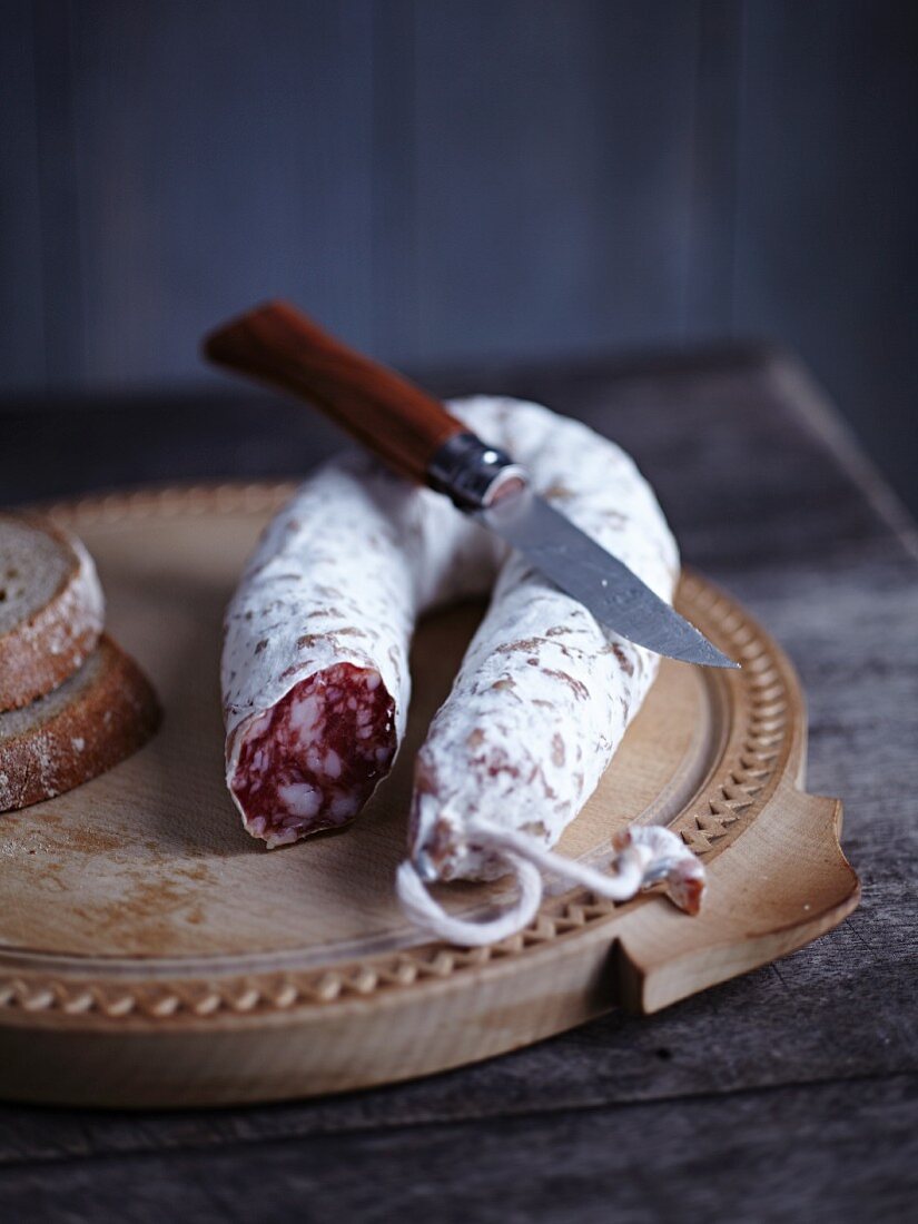 Salami mit Messer und Brot auf Holzteller