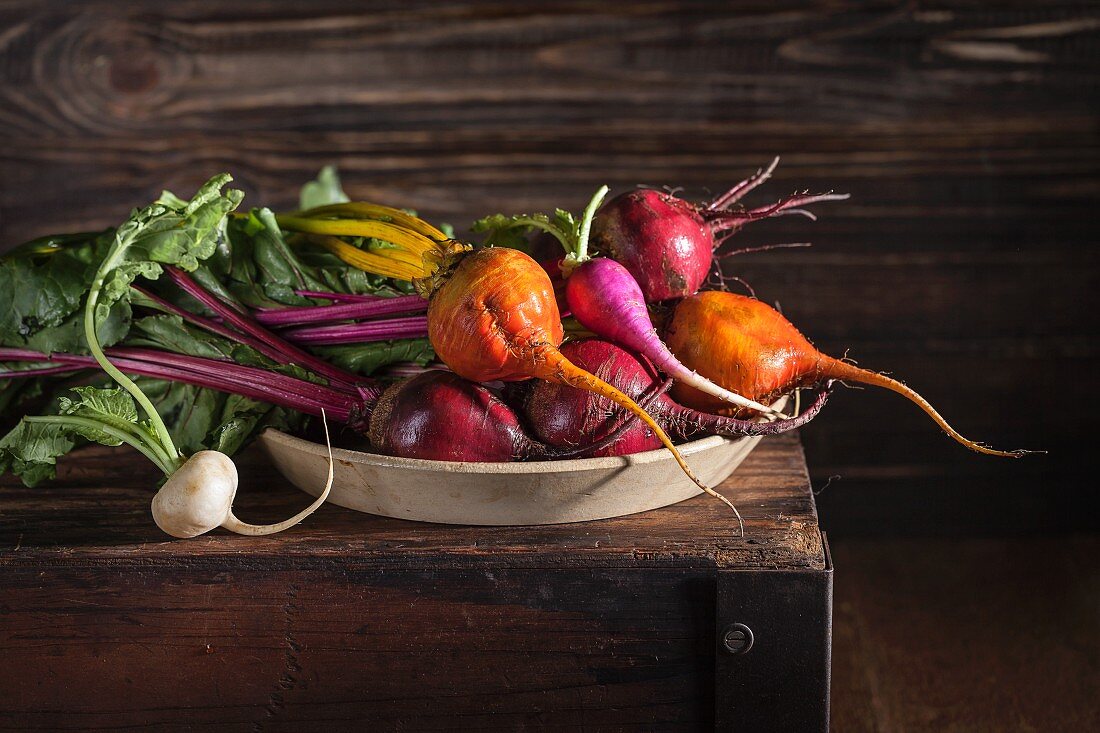 Fresh organic beetroot, golden beets and radishes in a bowl on top of an old wooden box