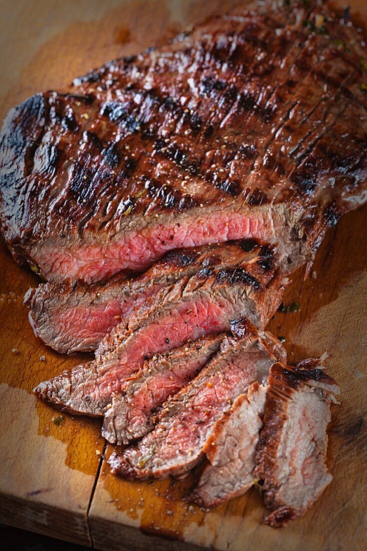 A flank steak, sliced, on a chopping board