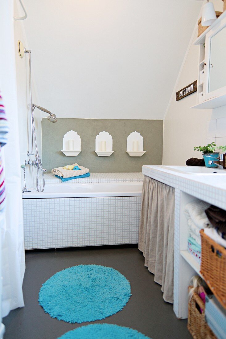 Bathtub with Oriental-style candle arrangement on wall; masonry washstand with baskets on open-fronted shelves to one side