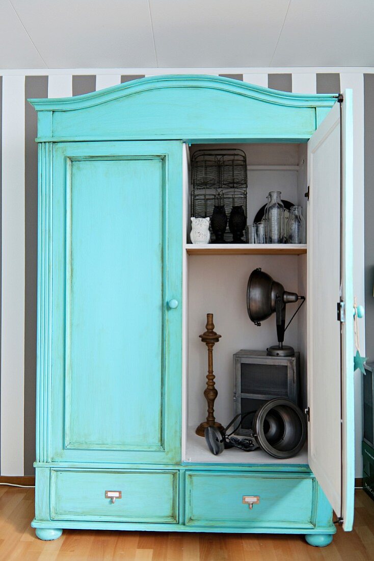 Vintage cupboard painted pastel turquoise with patinated surface; open door showing view of ornaments